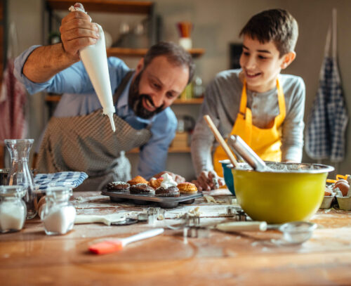 Photo of father and his son decorating cupcakes in the kitchen