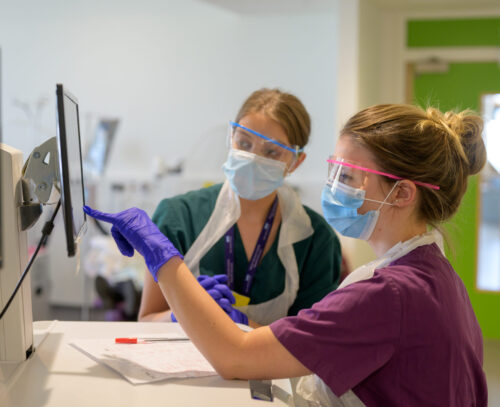 Two female NHS professionals looking at a computer monitor. One of them is pointing at the screen.