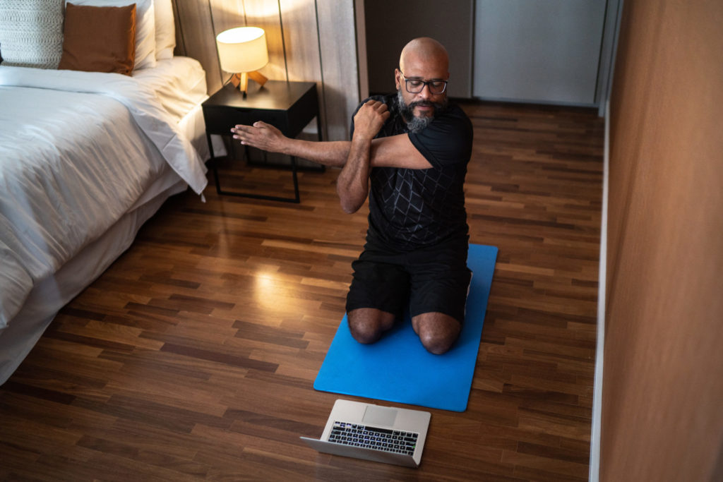 Mature man exercising at home - watching virtual exercise class on laptop