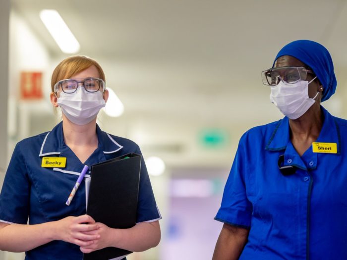 Two staff walk down corridor wearing PPE
