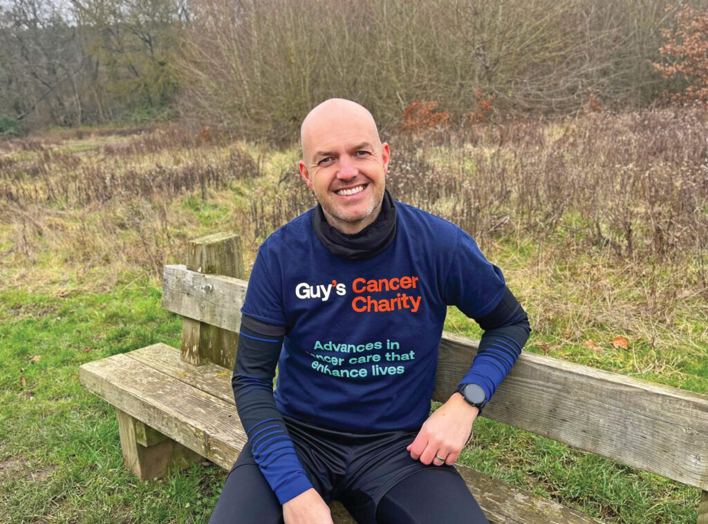 Gary sat on a wooden bench, wearing a navy t-shirt that reads 