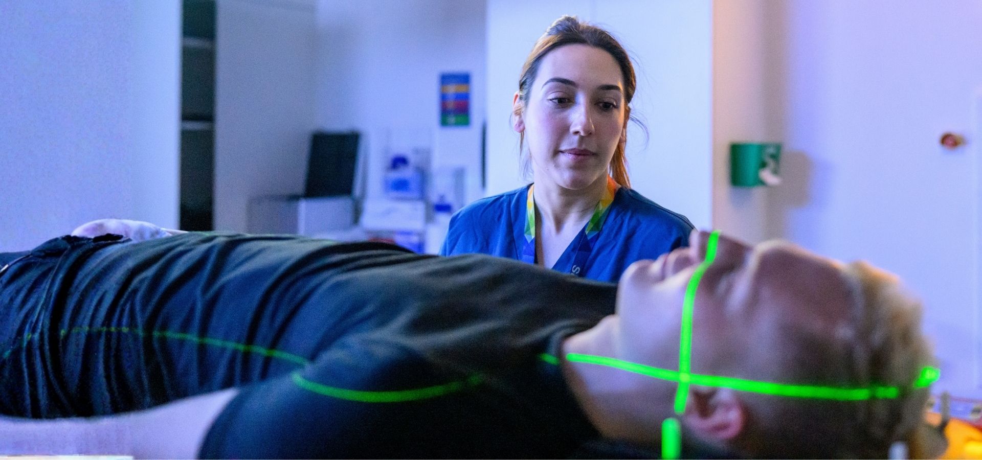 Guy's Cancer nurse using the HyperArc machine on patient, the patient is lying down and has green laser light scanning across his face.