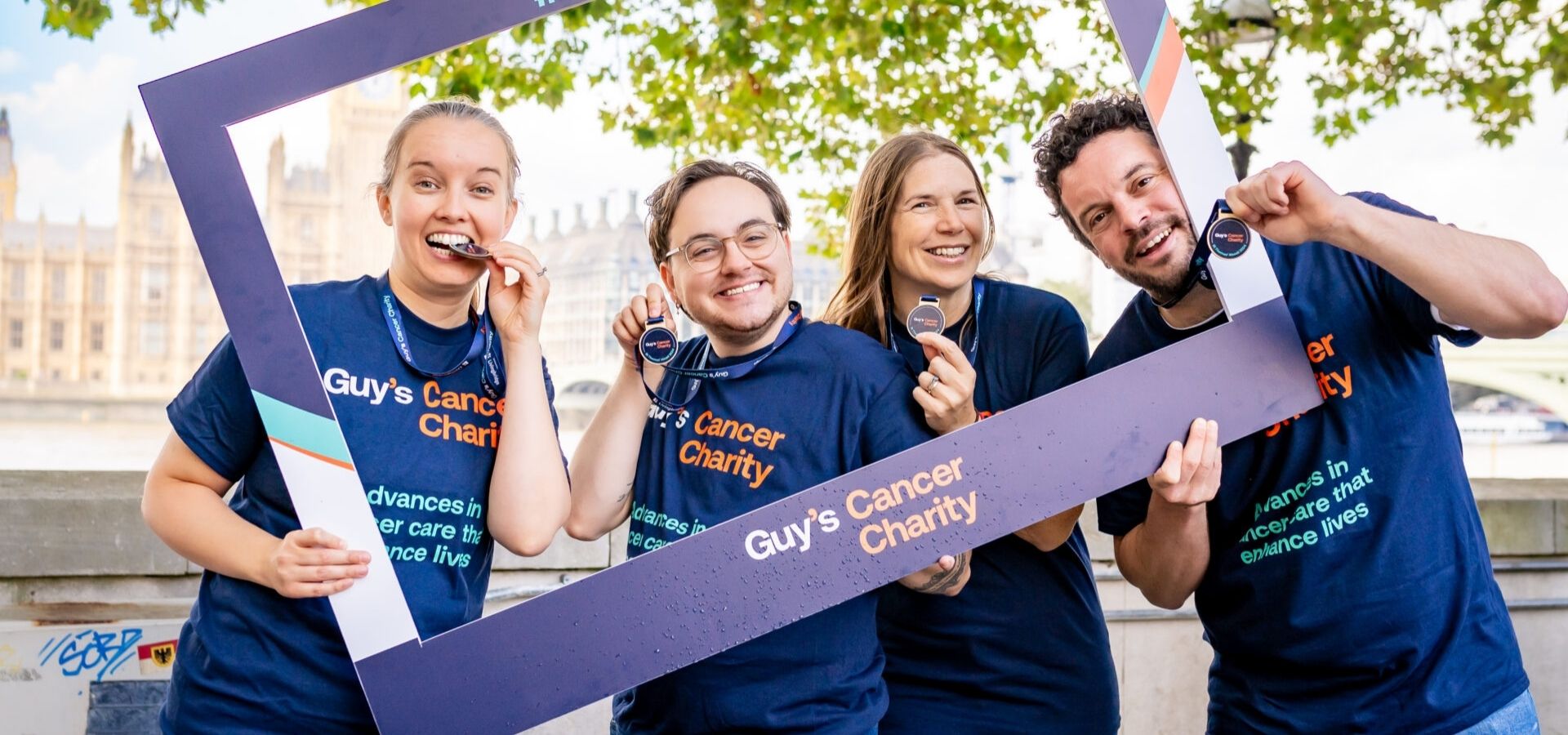 Image of a group holding a Guy's Cancer Charity photo prop, with their St Thomas' Abseil medals