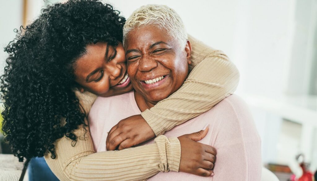 A woman hugging her family member from behind, both appear to be smiling.