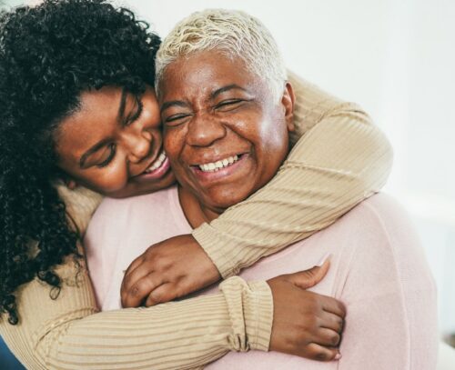 A woman hugging her family member from behind, both appear to be smiling.
