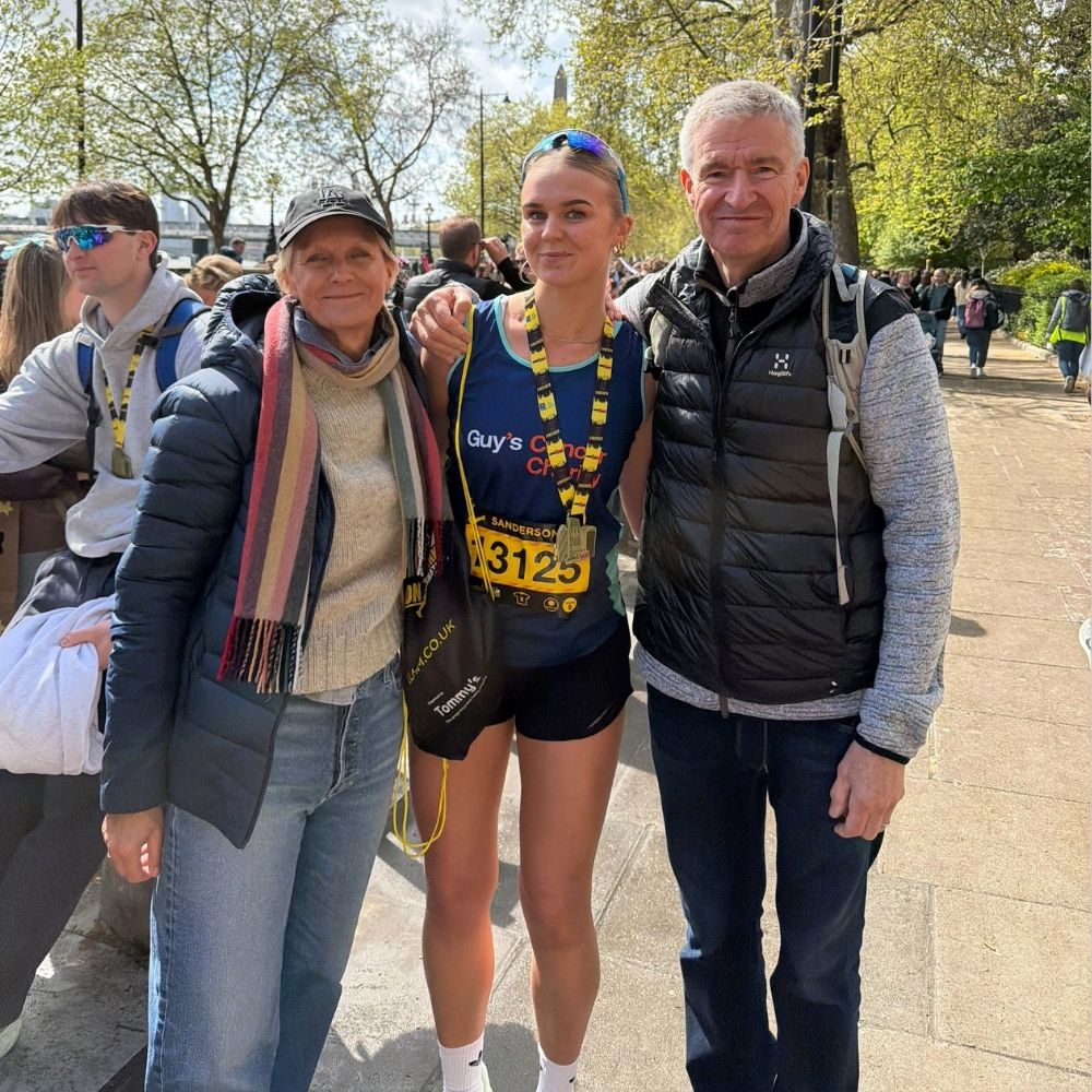 Lizzie with her parents after she completed the London Landmarks Half Marathon. Lizzie is in the middle wearing a medal and her parents are either side, there are fellow runners behind her.